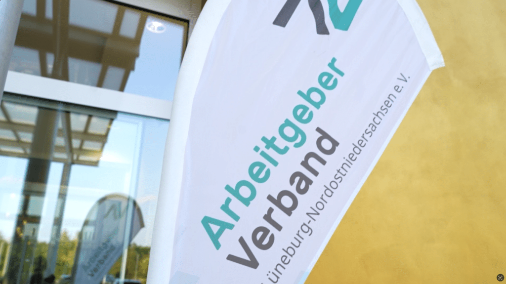 Weiße Fahne mit Text „Arbeitgeber Verband Lüneburg-Nordostniedersachsen e.V.“ bei einer Veranstaltung im Freien in der Nähe eines Gebäudes, Förderung effektiver Zeitmanagementprinzipien.